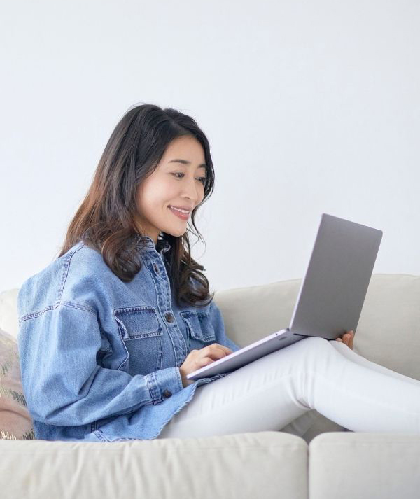Young woman looking and smiling at her laptop while sitting on the couch